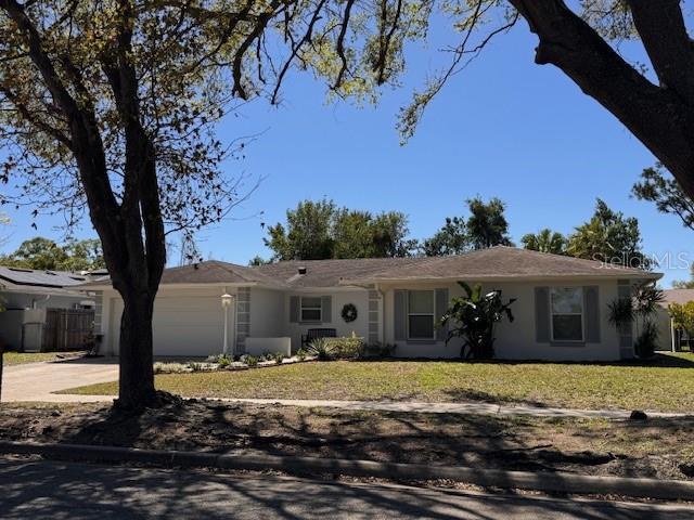 ranch-style home with a garage, a front yard, concrete driveway, and stucco siding