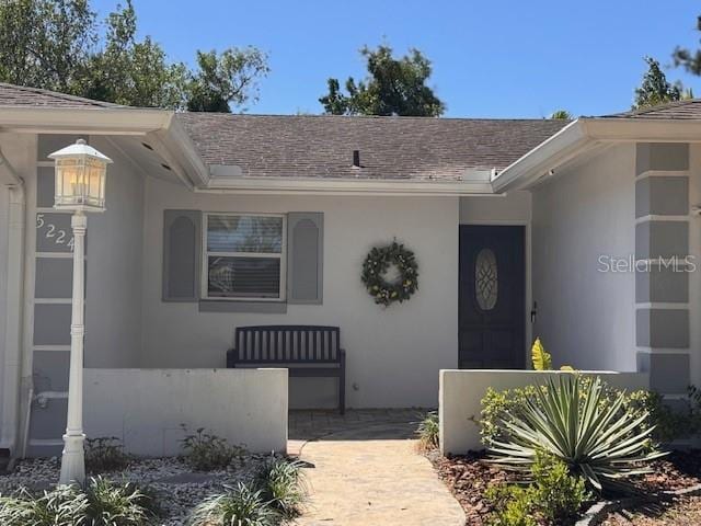 property entrance featuring a shingled roof and stucco siding