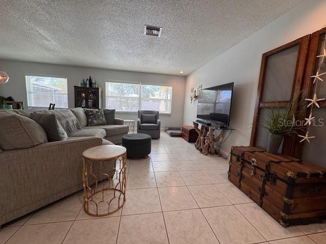 living room with a textured ceiling, light tile patterned flooring, plenty of natural light, and visible vents