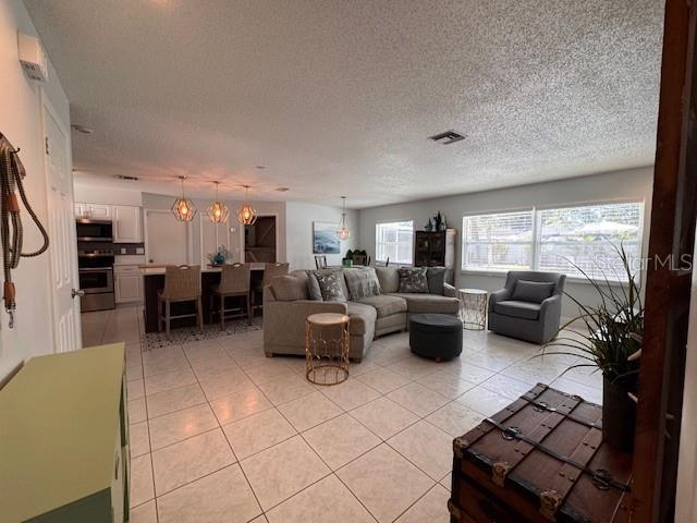 living room with visible vents, a notable chandelier, a textured ceiling, and light tile patterned floors