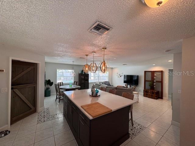 kitchen with light tile patterned floors, a kitchen island, visible vents, light countertops, and decorative light fixtures