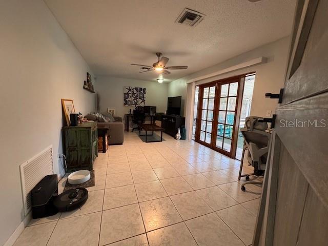 living area with light tile patterned flooring, ceiling fan, visible vents, and french doors