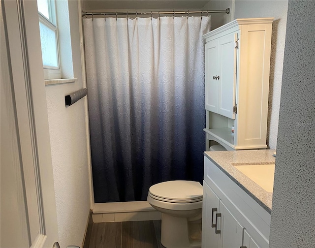 bathroom with toilet, wood finished floors, and a textured wall