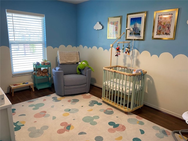 bedroom with a crib, wood finished floors, and baseboards