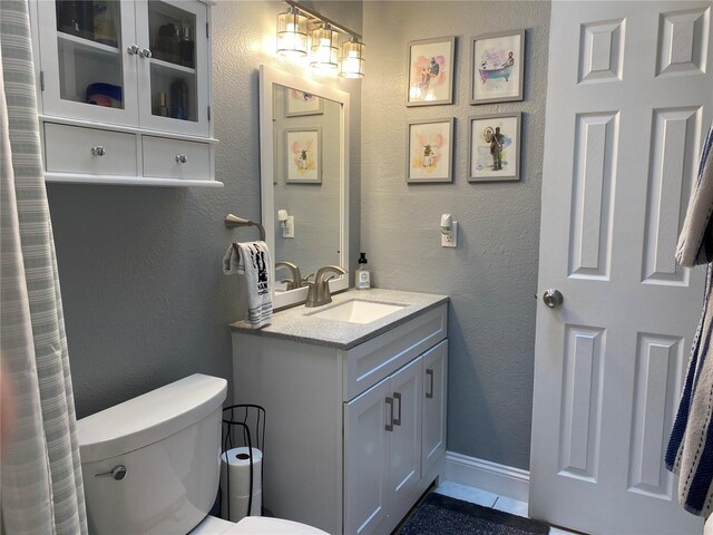 full bath with toilet, vanity, baseboards, and a textured wall