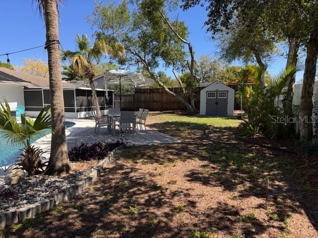 view of yard featuring an outbuilding, a patio, a storage unit, a sunroom, and fence