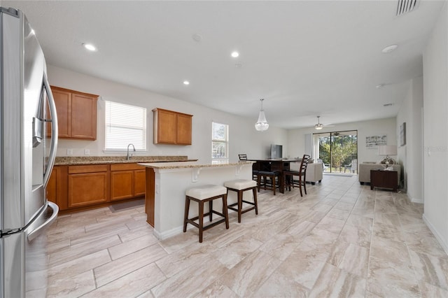 kitchen with stainless steel refrigerator with ice dispenser, visible vents, brown cabinetry, open floor plan, and a kitchen island