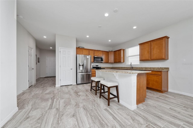 kitchen with brown cabinetry, a kitchen island, appliances with stainless steel finishes, a breakfast bar area, and a sink