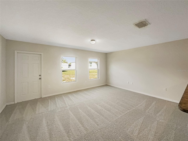 carpeted spare room with a textured ceiling, visible vents, and baseboards