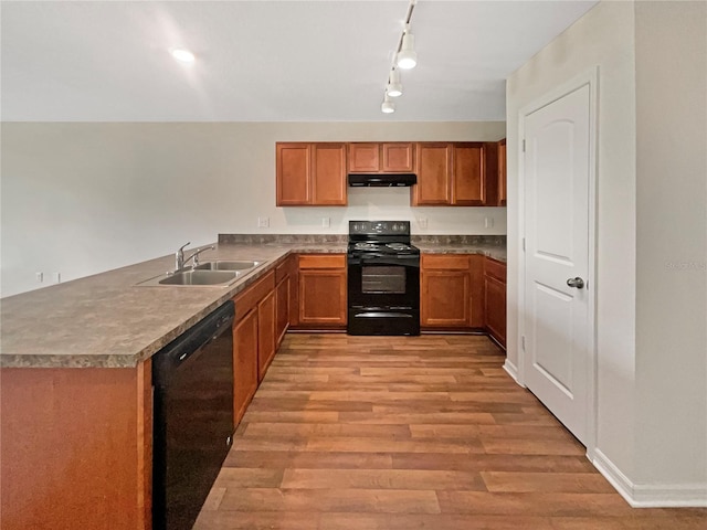 kitchen featuring under cabinet range hood, a sink, light wood-style floors, brown cabinets, and black appliances