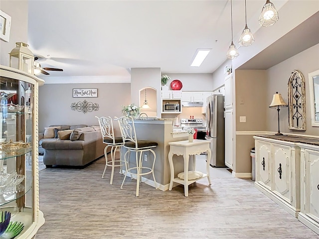 kitchen featuring light wood finished floors, stainless steel appliances, white cabinetry, a peninsula, and a kitchen breakfast bar