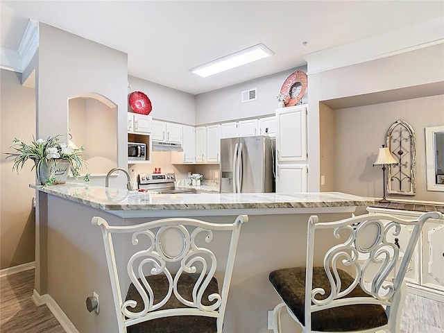 kitchen featuring light stone counters, visible vents, appliances with stainless steel finishes, under cabinet range hood, and a kitchen bar