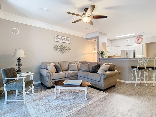 living area with wood finished floors, visible vents, a ceiling fan, baseboards, and crown molding