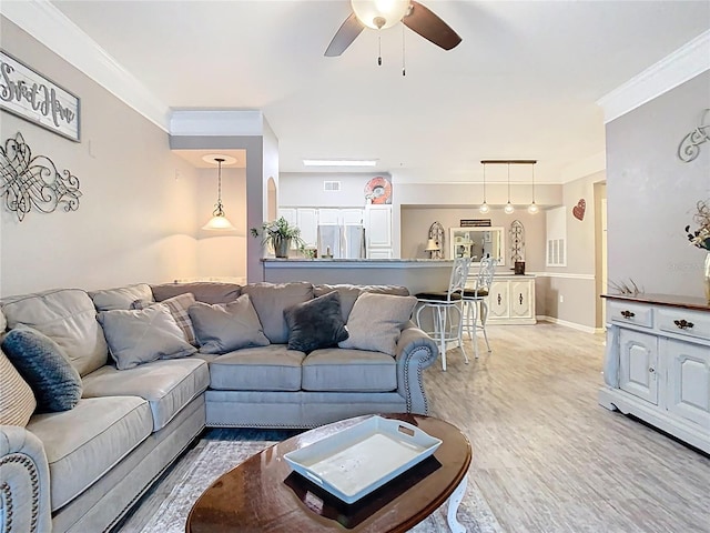 living area featuring visible vents, baseboards, a ceiling fan, ornamental molding, and light wood-style floors