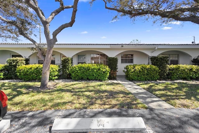 view of front of house featuring a tiled roof, a front yard, and stucco siding