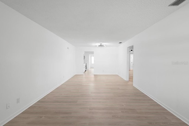 empty room with baseboards, light wood-style flooring, visible vents, and a textured ceiling