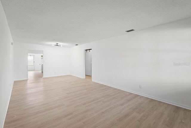 unfurnished room featuring visible vents, baseboards, a textured ceiling, and light wood finished floors