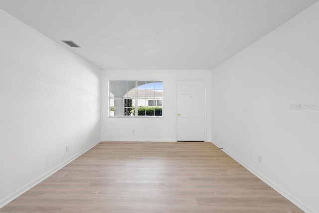 unfurnished room with baseboards, visible vents, light wood-style flooring, and a textured ceiling