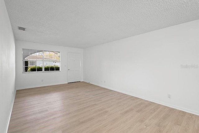 empty room featuring light wood-type flooring, visible vents, a textured ceiling, and baseboards