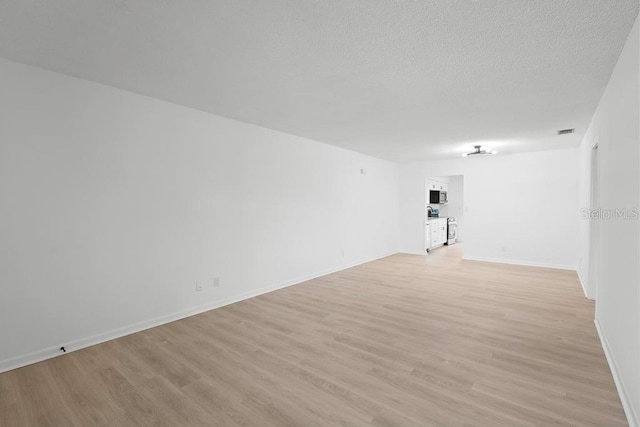 spare room with light wood-style floors, visible vents, a textured ceiling, and baseboards