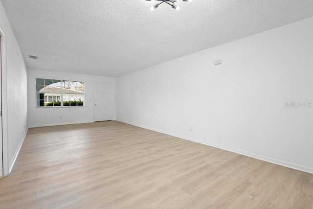 empty room featuring baseboards, visible vents, a textured ceiling, and light wood finished floors