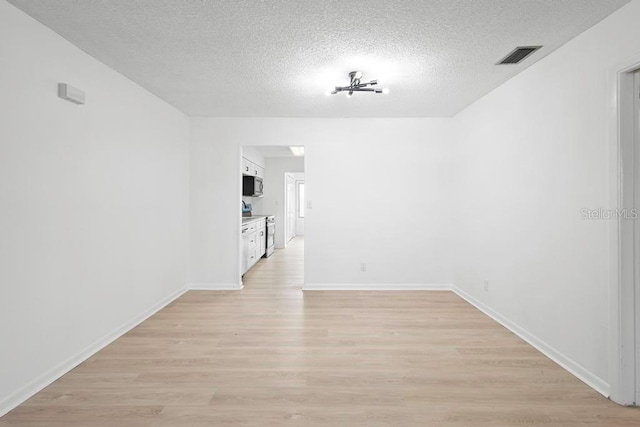 spare room with a textured ceiling, baseboards, visible vents, and light wood-style floors