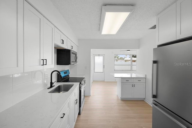 kitchen with tasteful backsplash, stainless steel appliances, light wood-type flooring, white cabinetry, and a sink