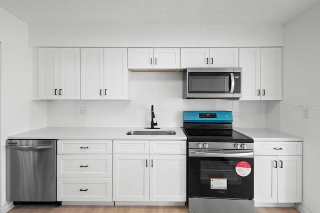 kitchen with light countertops, appliances with stainless steel finishes, a sink, and white cabinets