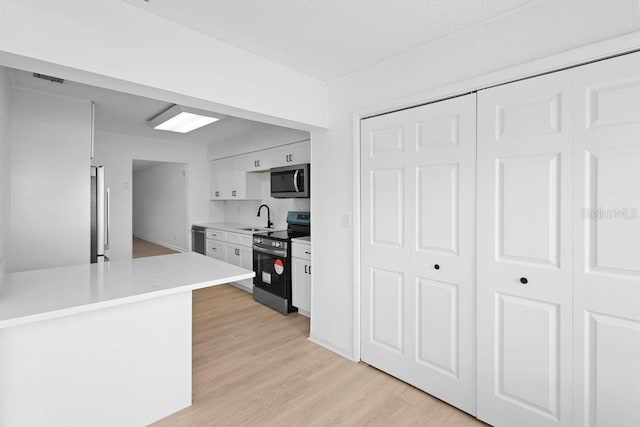 kitchen with a sink, white cabinetry, light countertops, appliances with stainless steel finishes, and light wood finished floors