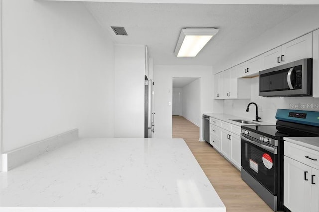 kitchen featuring light wood finished floors, visible vents, appliances with stainless steel finishes, white cabinets, and a sink