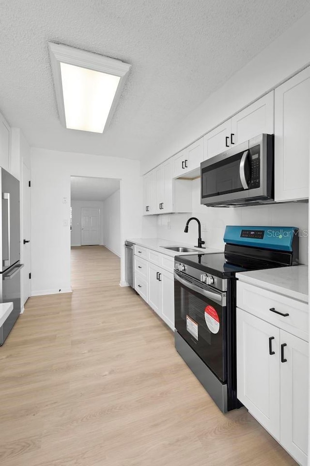 kitchen with stainless steel appliances, a sink, light countertops, and white cabinetry