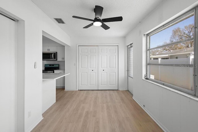 interior space featuring a textured ceiling, visible vents, baseboards, a closet, and light wood finished floors