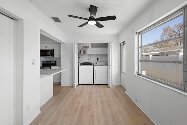 kitchen featuring visible vents, washing machine and clothes dryer, stainless steel appliances, a textured ceiling, and light wood-type flooring