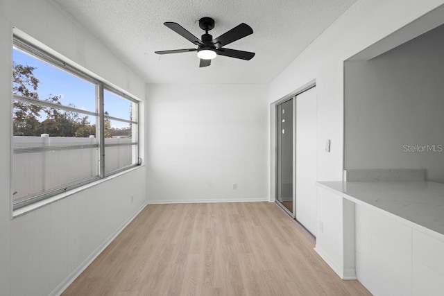 unfurnished room featuring light wood finished floors, ceiling fan, baseboards, and a textured ceiling