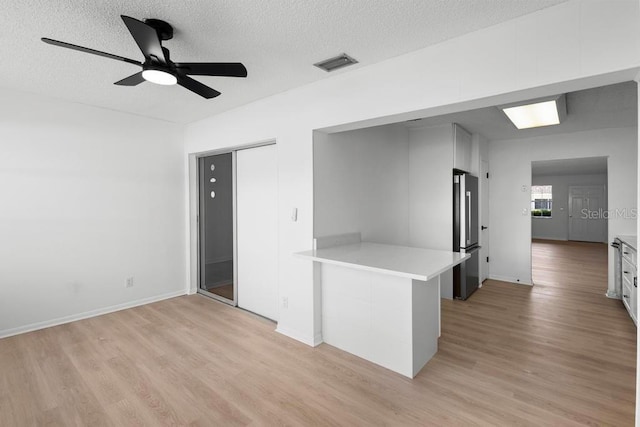 spare room with a textured ceiling, ceiling fan, visible vents, baseboards, and light wood finished floors