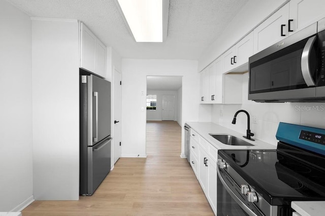 kitchen featuring light wood finished floors, appliances with stainless steel finishes, a sink, and white cabinetry