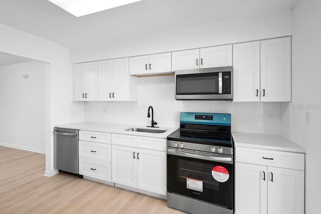 kitchen with light wood finished floors, stainless steel appliances, light countertops, white cabinetry, and a sink