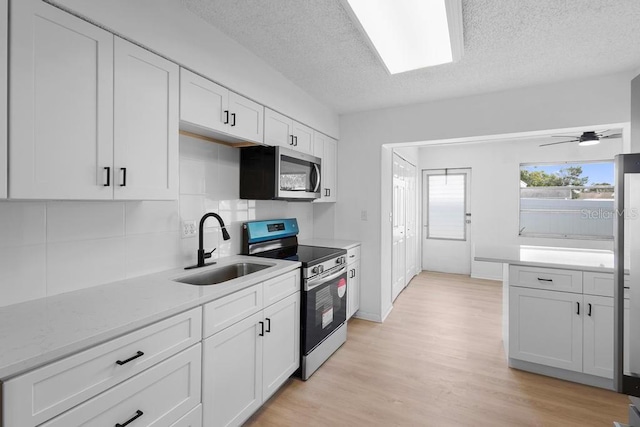 kitchen with a textured ceiling, a sink, white cabinetry, appliances with stainless steel finishes, and light wood finished floors