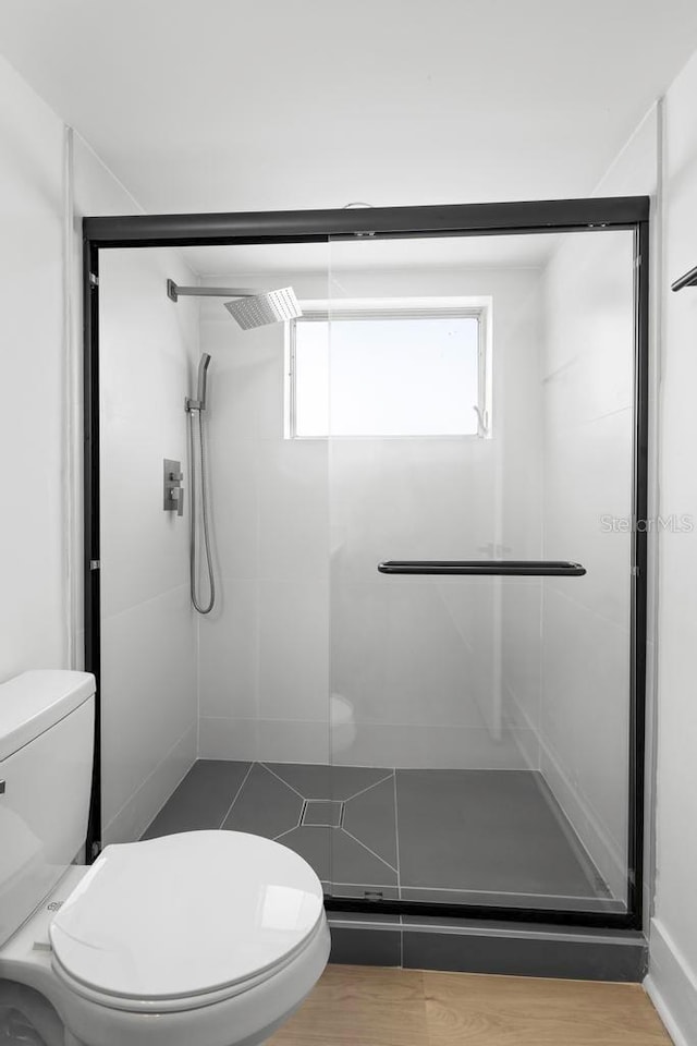 bathroom featuring wood finished floors, a shower stall, and toilet