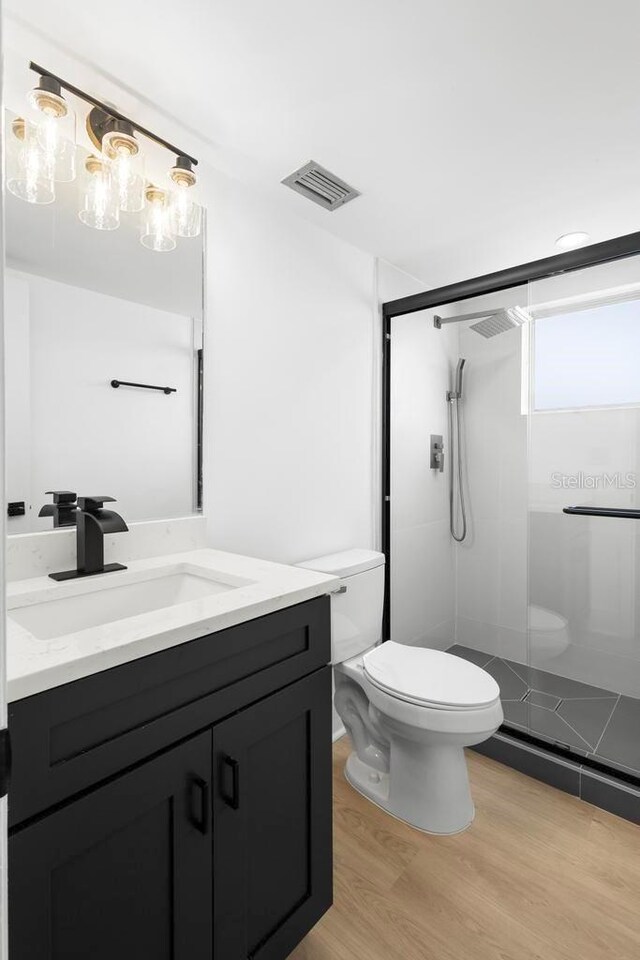 full bathroom featuring toilet, wood finished floors, vanity, visible vents, and a stall shower