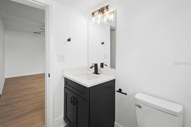 half bathroom featuring toilet, baseboards, wood finished floors, and vanity