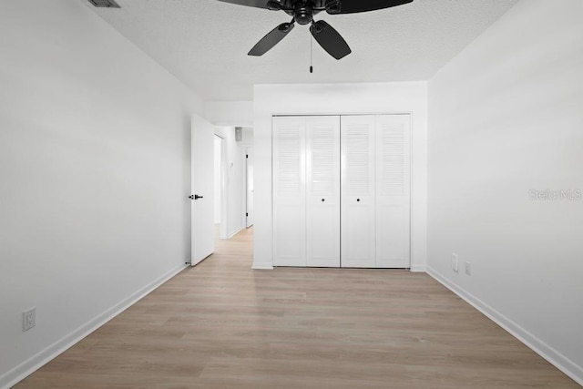 unfurnished bedroom featuring a textured ceiling, a closet, light wood-type flooring, and baseboards