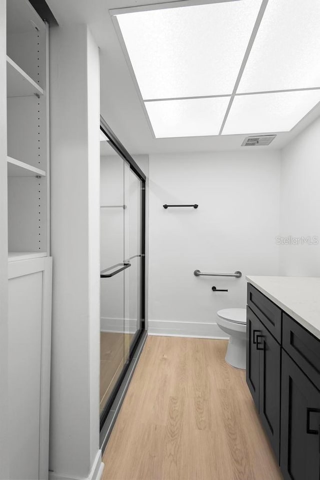 bathroom with a stall shower, visible vents, toilet, wood finished floors, and vanity