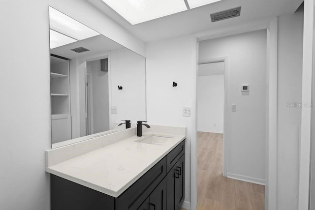 bathroom with visible vents, vanity, baseboards, and wood finished floors