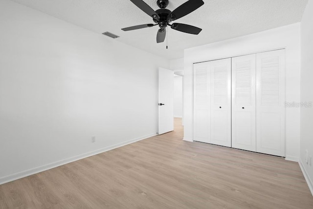 unfurnished bedroom featuring light wood-type flooring, visible vents, a textured ceiling, and baseboards