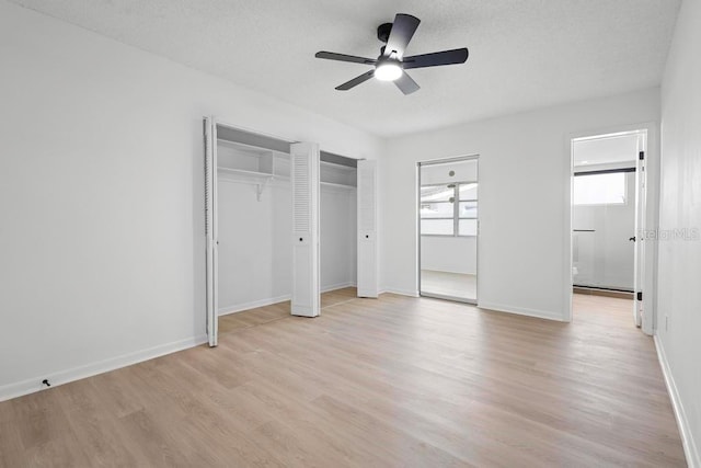 unfurnished bedroom featuring a textured ceiling, multiple closets, baseboards, light wood-style floors, and ensuite bath