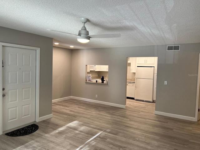 spare room with visible vents, light wood-style flooring, a ceiling fan, a textured ceiling, and baseboards