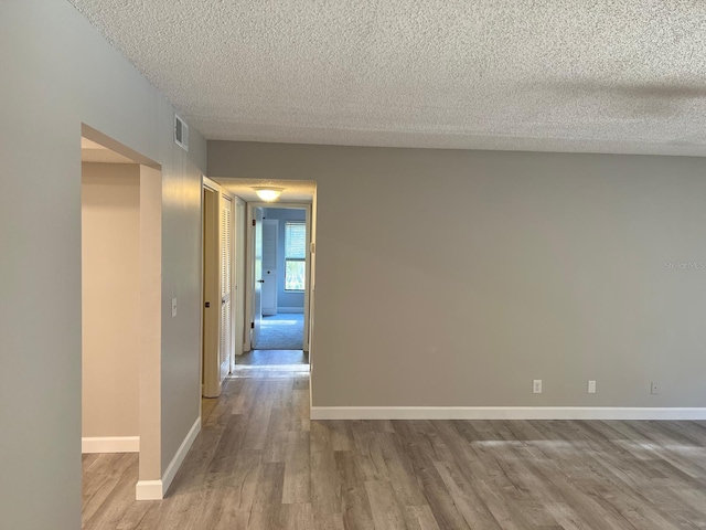 hallway with a textured ceiling, wood finished floors, visible vents, and baseboards