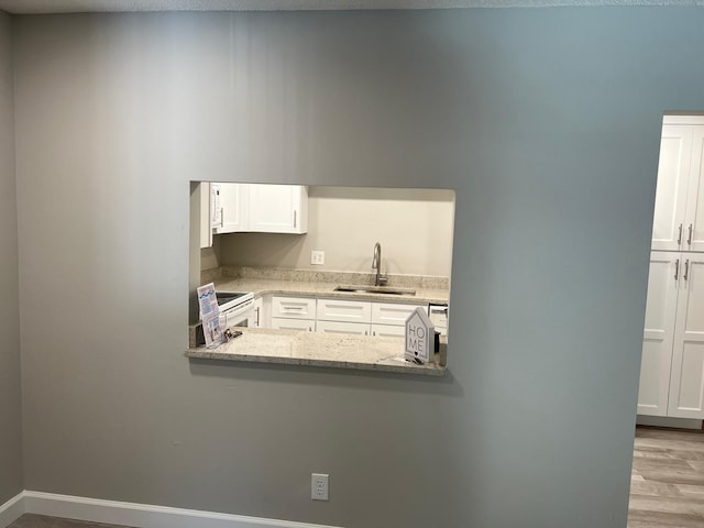 kitchen with wood finished floors, a sink, baseboards, white cabinets, and white electric range oven