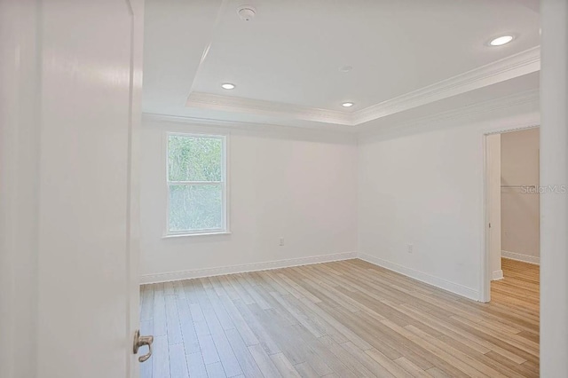 empty room featuring light wood-type flooring, a raised ceiling, crown molding, and baseboards